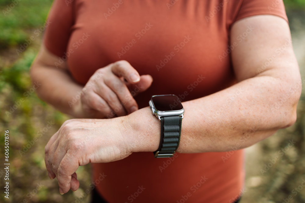 Portrait of a happy active beautiful senior caucasian woman runner running while checking heart rate at park, female in sport cloth jogging while looking on watch at park, healthy sport active