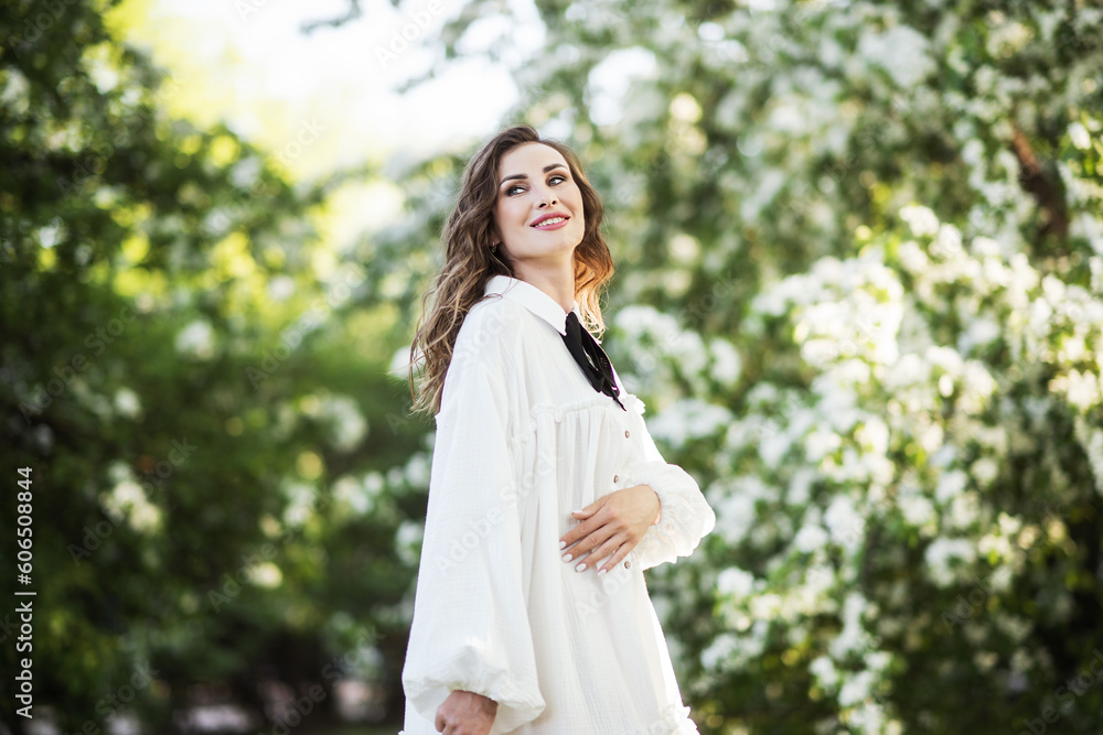 Portrait of a beautiful young girl in a white dress. A girl poses near a blooming white tree. She enjoys the smell of flowers in the apple orchard. Portrait of a beautiful young girl in a white dress. A girl poses near a blooming white tree. She enjoys the smell of flowers in the apple orchard.