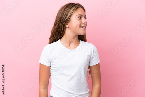 Little caucasian girl isolated on pink background looking to the side and smiling