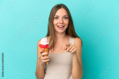 Young Lithuanian woman with cornet ice cream isolated on blue background surprised and pointing front