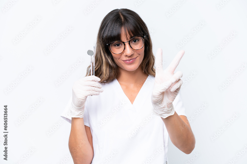 Dentist caucasian woman holding tools isolated on white background smiling and showing victory sign Dentist caucasian woman holding tools isolated on white background smiling and showing victory sign