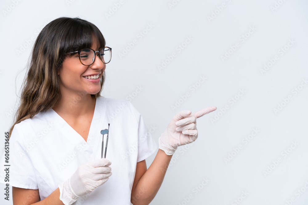 Dentist caucasian woman holding tools isolated on white background pointing finger to the side and presenting a product Dentist caucasian woman holding tools isolated on white background pointing finger to the side and presenting a product