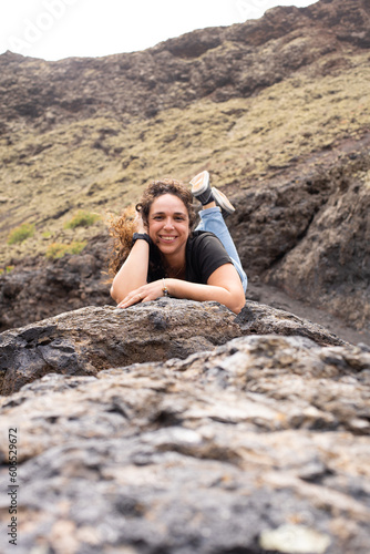 young brunette woman smiling inside the Volcán del Cuervo in Lanzarote, Spain, wearing blue jeans, black trainers and black sneakers