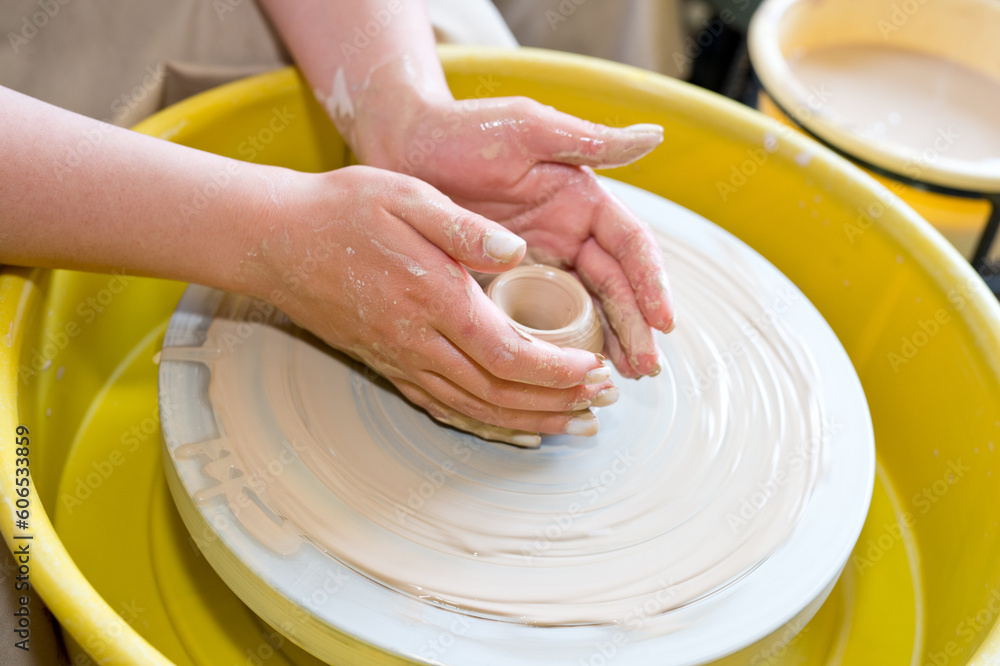 The hands of a potter sculpting a piece of clay on a rotating potter's wheel.