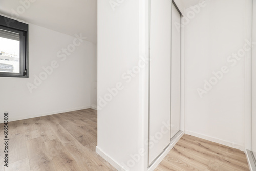 An empty bedroom with a dressing room with white wooden cabinets