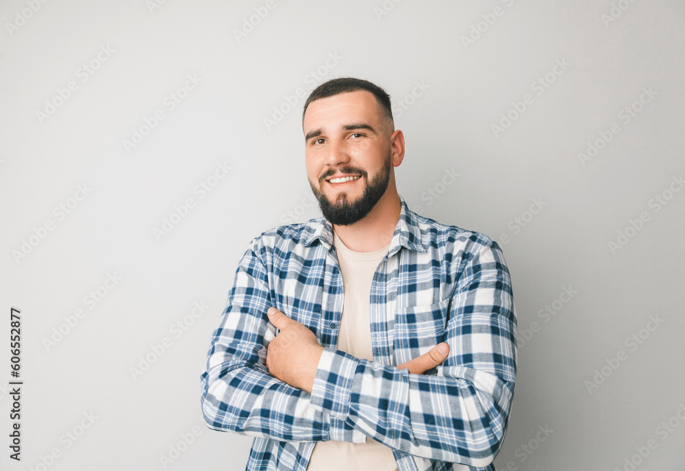 Confident young handsome man in shirt keeping arms crossed and smiling while standing against gray background Confident young handsome man in shirt keeping arms crossed and smiling while standing against gray background
