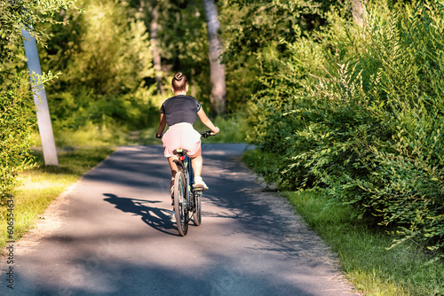 A young woman riding a bicycle in a park in summer in the sunny morning.