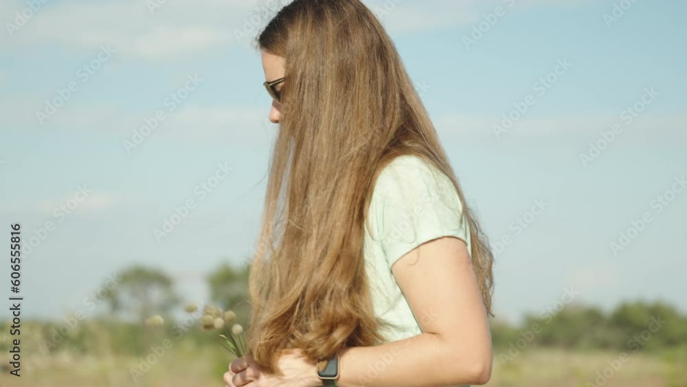 A woman with long hair walks through a sunlit field during the day, holding a bouquet of Lagurus plants in her hands. A woman with long hair walks through a sunlit field during the day, holding a bouquet of Lagurus plants in her hands.