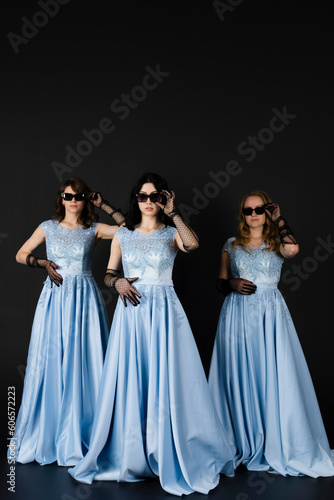 Group of three bridesmaids in blue dresses and black sunglasses. isolated on black background.