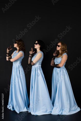 Group of three bridesmaids in blue dresses and black sunglasses. isolated on black background.