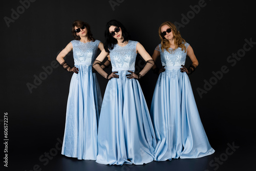 Group of three bridesmaids in blue dresses and black sunglasses, posing. isolated on black background.