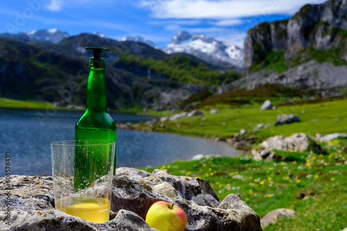 Green bottle and glass of natural Asturian cider made from fermented apples with view on Covadonga lake and tops of Picos de Europa mountains, Spain photo