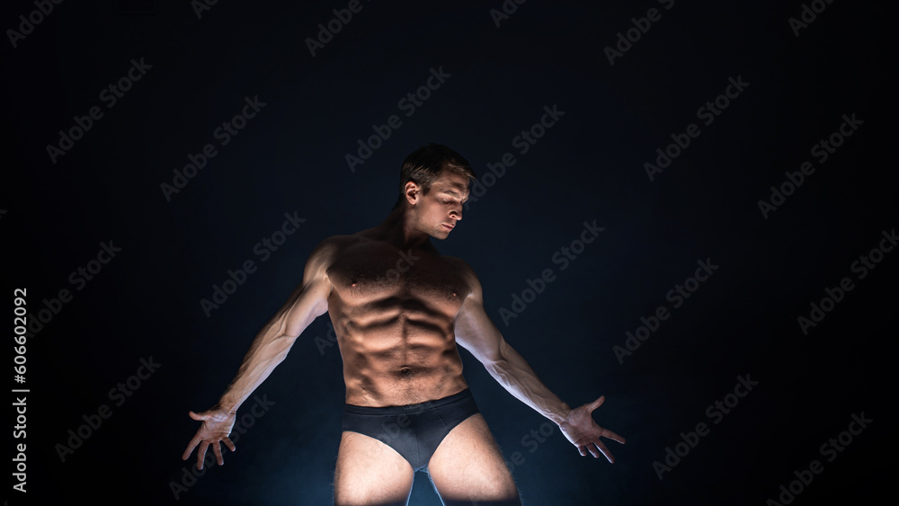 Muscular athlete in an epic pose, dark background, bright light from below, the concept of sports and bodybuilding