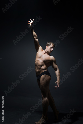 A muscular athlete stretches his arm up, striving for the ideal, a concept. Contrast photo on dark