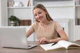 Online learning. Smiling teenage girl with laptop at wooden table indoors