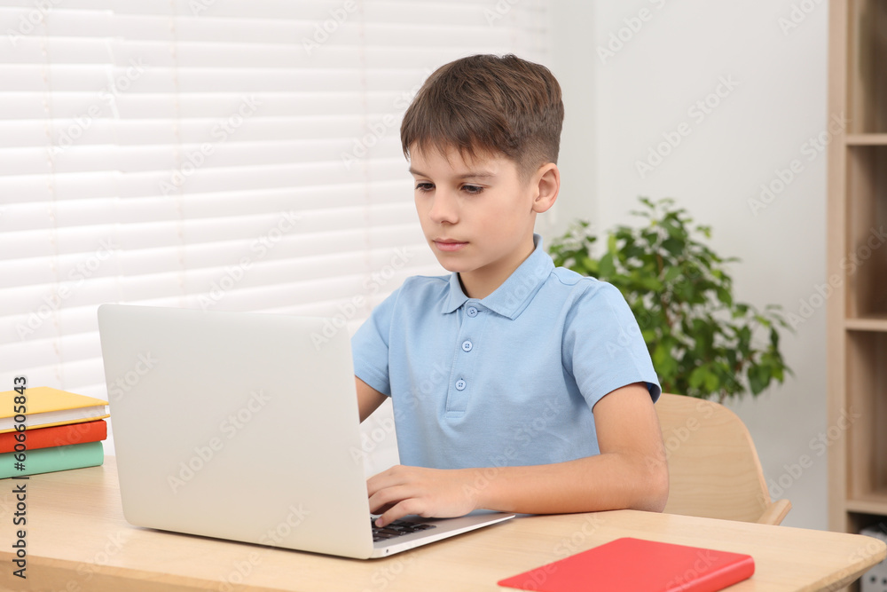 Boy using laptop at desk in room. Home workplace