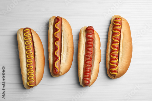 Fresh delicious hot dogs with sauces on white wooden table, flat lay