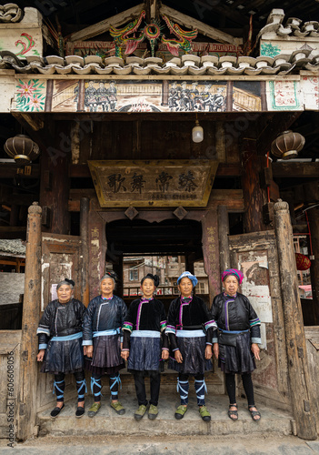 A singing group of 5 ethnic Kam women stand in front of the wooden drum tower in Xiaohuang village, Congjiang county, Guizhou, China.