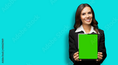 Portrait of happy smiling brunette businesswoman showing tablet pc, touchpad, with green chroma key screen, on aqua marine background. Confident attractive business woman at office.