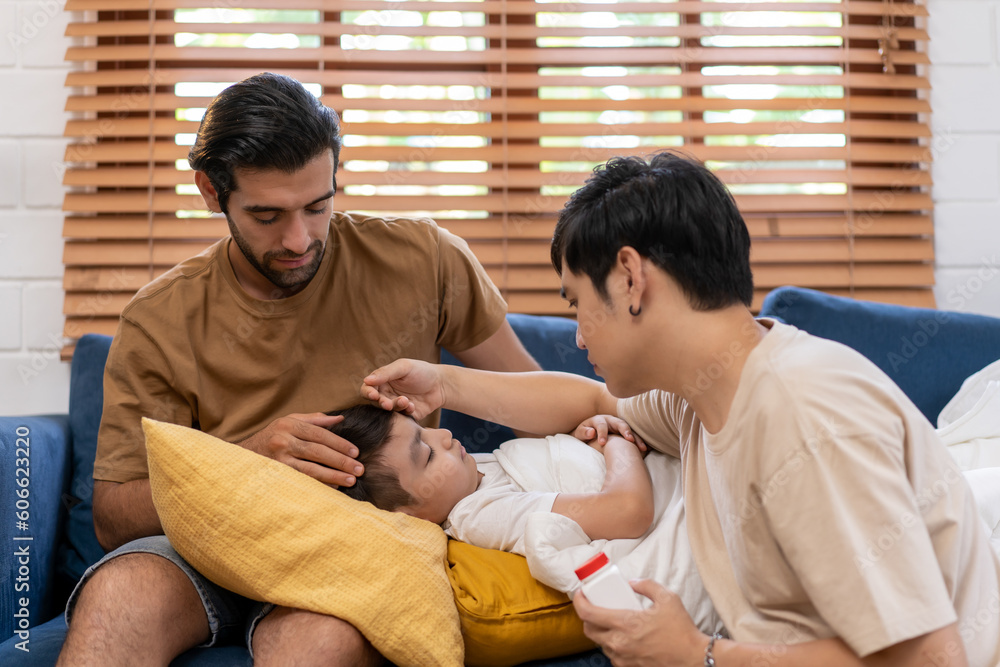 Fototapeta premium Diversity of a couple man touching the forehead of a sick little boy son at home, caring parent father checking child’s temperature with his hand.