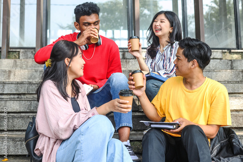 Diverse millennial young college students smiling enjoying pleasant conversation in campus staircase while drinking a cup of coffee