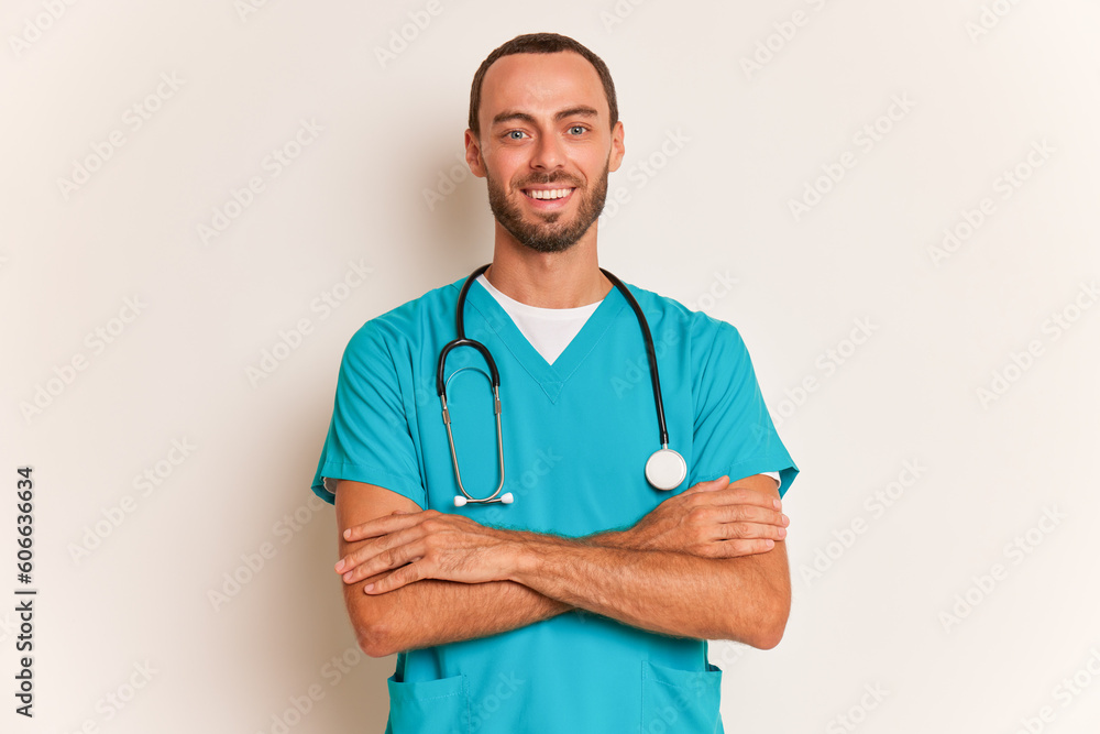 Young bearded man holding his hands crossed on his chest looking at camera and smiling, wears special medical shirt, professional people concept, copy space Young bearded man holding his hands crossed on his chest looking at camera and smiling, wears special medical shirt, professional people concept, copy space