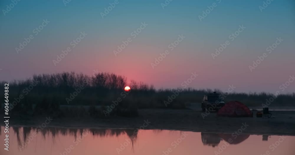 The SUV stands next to a stretched awning on the shore of the lake, surrounded by trees at sunset The SUV stands next to a stretched awning on the shore of the lake, surrounded by trees at sunset