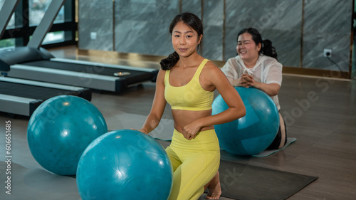 Humor in sports Ball Yoga. Fat Asian woman with her Yoga Instrutor teacher training in gymnastics with fitness ball.
