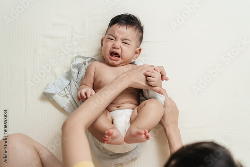 Top view crying Asian baby wearing clothes by his mother. Concept babies healthcare.