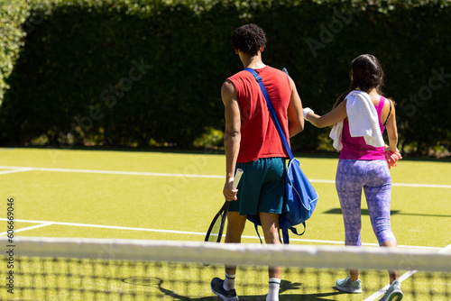 Rear view of biracial young couple walking out of tennis court after playing game