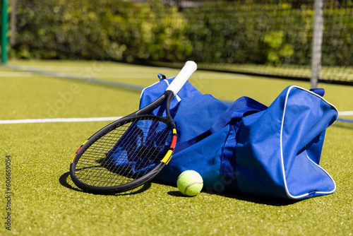 Blue gym bag with tennis racket and ball on grassy field at tennis court, copy space