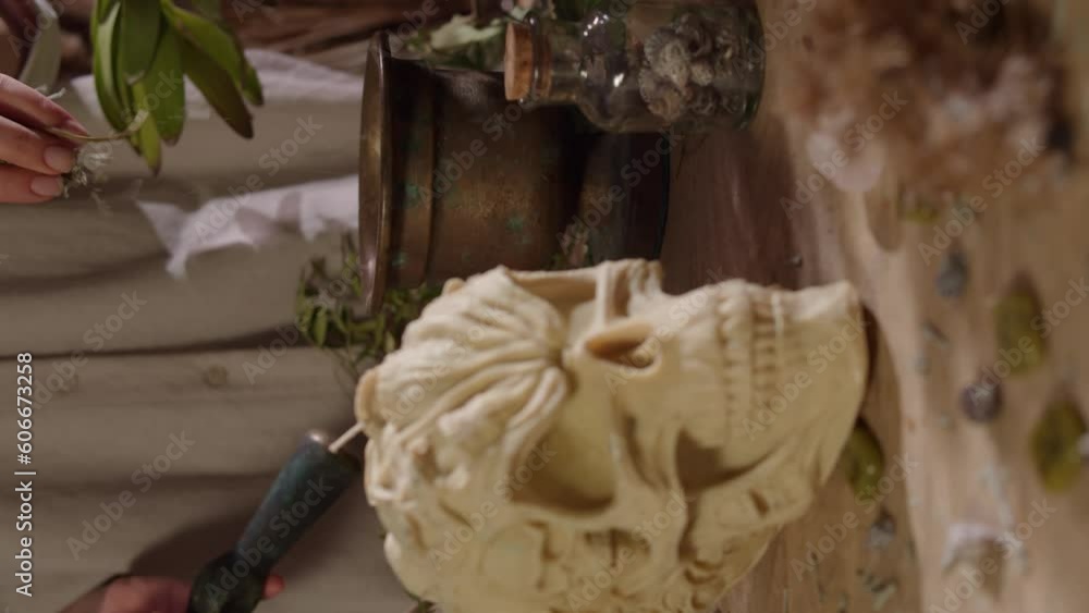 vertical shot of a girl chopping herbs in a mortar for occult rites. a table decorated with magic objects. Herbs, occult candles, magic stones and crystals. vertical shot of a girl chopping herbs in a mortar for occult rites. a table decorated with magic objects. Herbs, occult candles, magic stones and crystals.