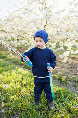 A three-year-old boy runs through a blooming garden with soap bubbles. Cheerful emotional child is walking in the park. Soap bars for children