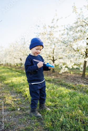 A three-year-old boy runs through a blooming garden with soap bubbles. Cheerful emotional child is walking in the park. Soap bars for children