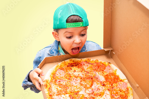 A seven year old fashionable boy in a green cap screaming in shock holds an open pizza box isolated on background.