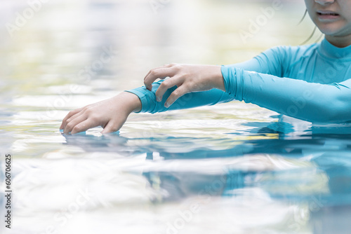 Asian teen girl having itchy or irritated skin,dry skin problem,scratching her body in swimming pool,young woman in swimsuit has an allergic reaction to chlorine in water,sensitive skin,health care