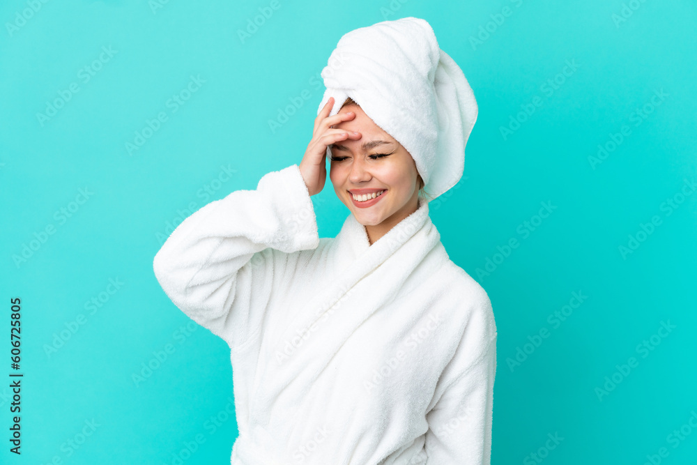 Teenager blonde girl in a bathrobe over isolated blue background smiling a lot Teenager blonde girl in a bathrobe over isolated blue background smiling a lot