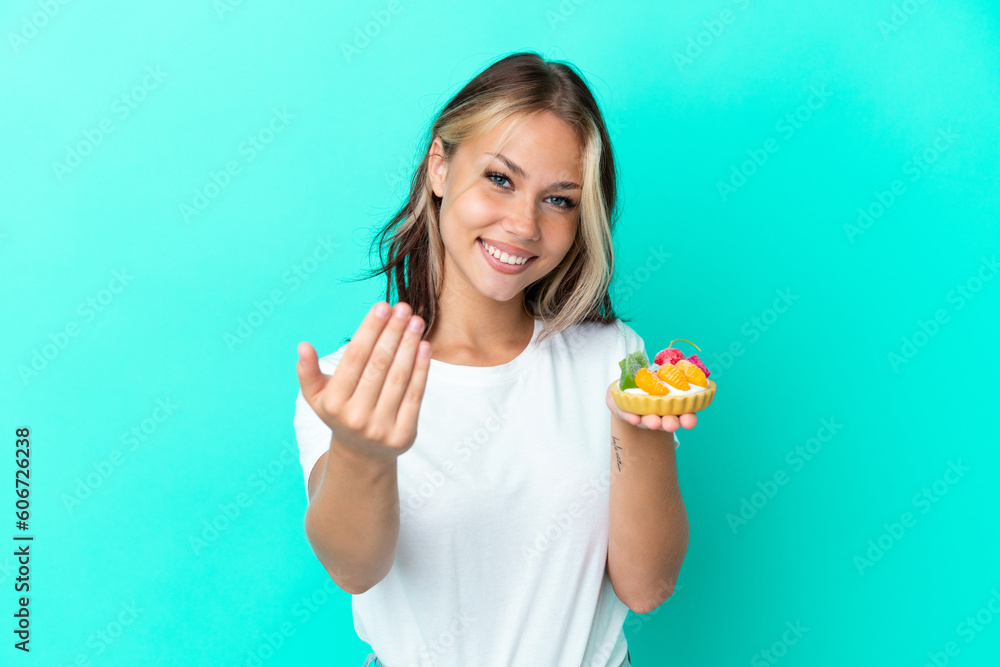 Young Russian woman holding a fruit sweet isolated on blue background inviting to come with hand. Happy that you came Young Russian woman holding a fruit sweet isolated on blue background inviting to come with hand. Happy that you came