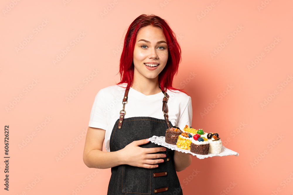 Pastry chef holding a muffins isolated on pink background laughing Pastry chef holding a muffins isolated on pink background laughing
