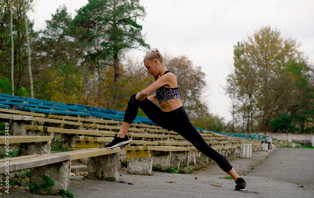 a girl in black clothes goes in for sports, does a stretch on a bench,Happy young woman doing stretching, outdoors, dressed in black suit