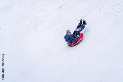 Teen boy sliding downhill on tube. Kid sledding in winter slope.