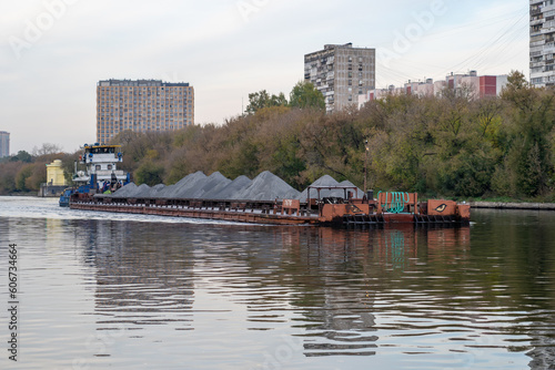 Barge loaded with sand or grey gravel floats on wide river