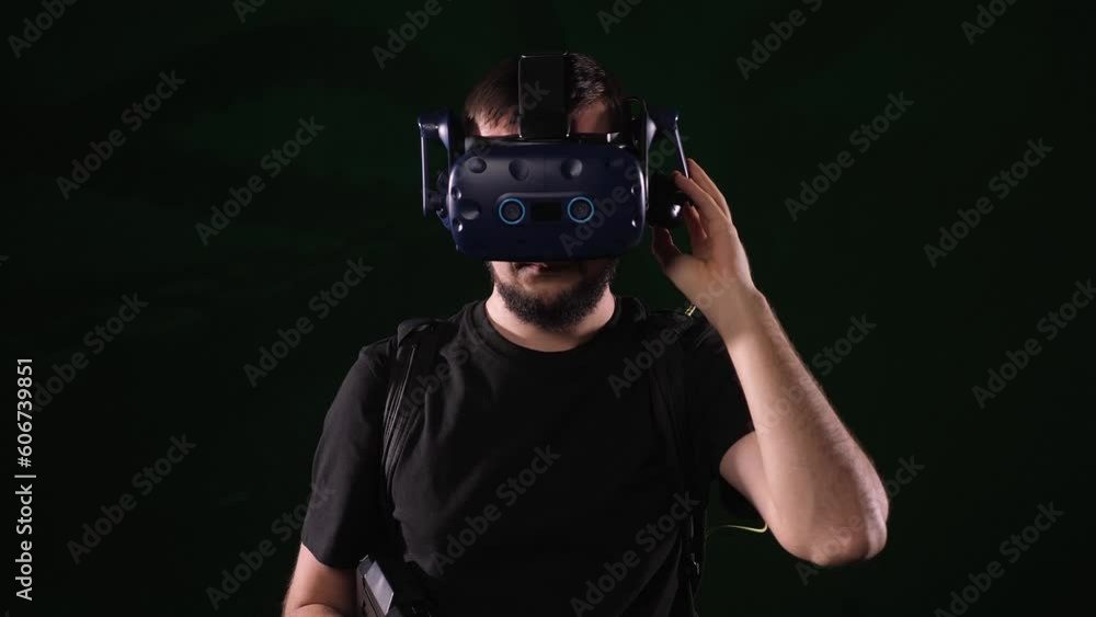A man in virtual reality glasses with a joystick in his hands is playing a virtual game on a black background. An active male gamer shoots from a machine gun in a virtual reality gaming studio. A man in virtual reality glasses with a joystick in his hands is playing a virtual game on a black background. An active male gamer shoots from a machine gun in a virtual reality gaming studio.