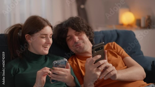 young couple lying on couch at home after work and both looking in their smartphones. people spending time together but with own phones, looking and posting social networks, messagers photo