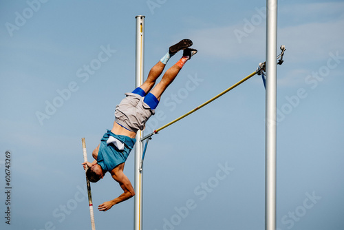 male athlete jumping pole vault in summer athletics championships on background blue sky