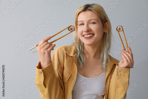 Young woman with sushi rolls on light background, closeup