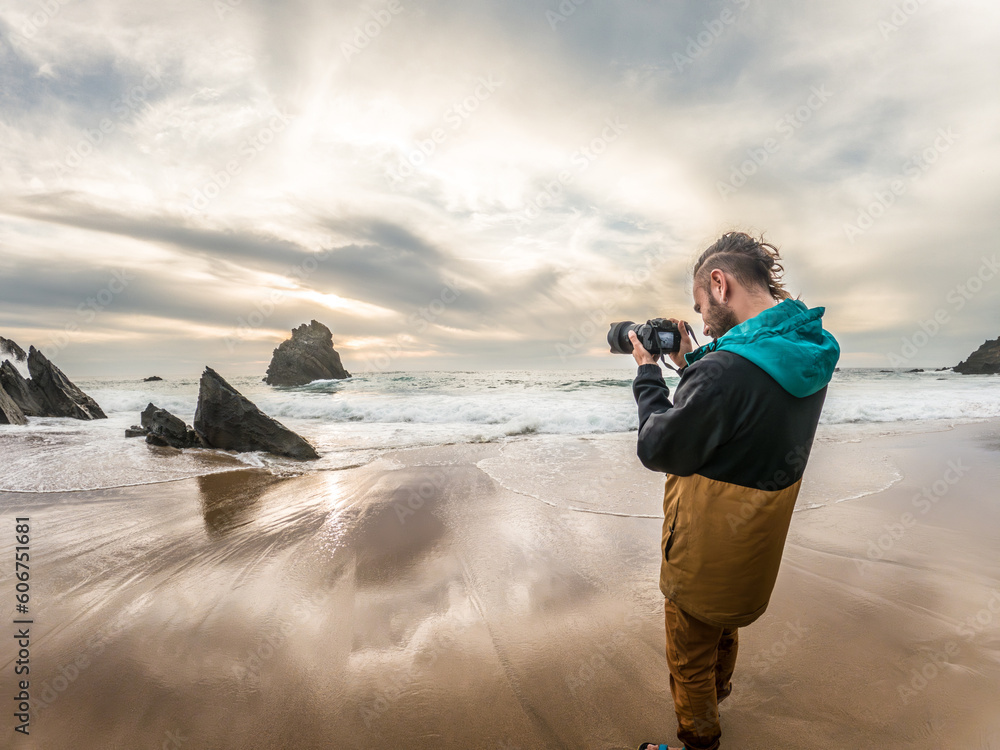 man taking pictures in nature at sunset on the beach with camera, rocks and clouds
