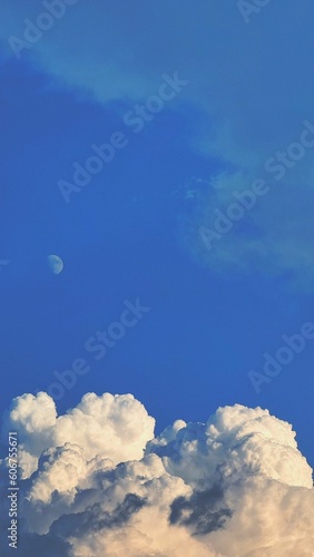 Vertical shot of the Moon against a cloudy bright blue sky perfect for wallpapers