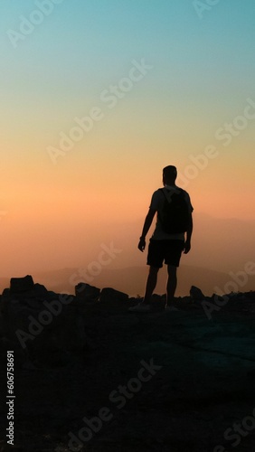 Vertical shot of a silhouette of a male on a cliff at sunset