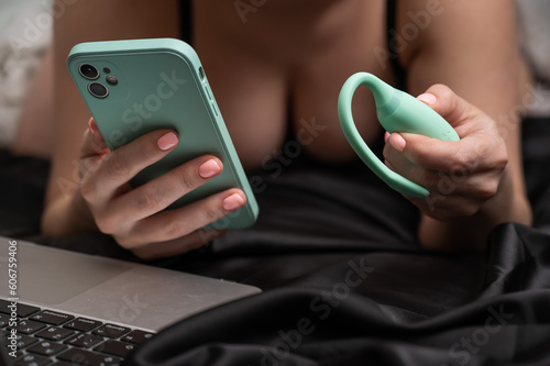 A woman lies on a bed and synchronizes the kegel machine with a smartphone. photo